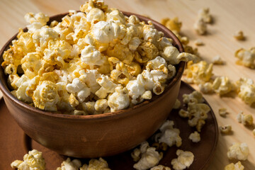 Caramel popcorn in a brown clay bowl on a wooden table top.