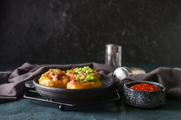 Frying pan with baked potato and sauce on dark background