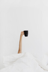Woman's hand laying in bed and holding mug with coffee.
