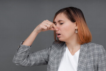 Young woman feels disgust pinches her nose with fingers because of unpleasant stink.