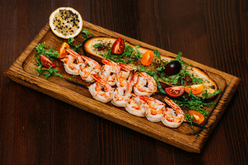 Fototapeta na wymiar Seafood. Shellfish. Delicious grilled shrimp with bruschetta and fresh vegetables and lemon on a wooden background