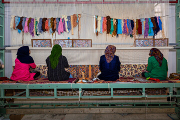 Iranian women waving Persian rugs in the carpet workshop in Naein, Iran.