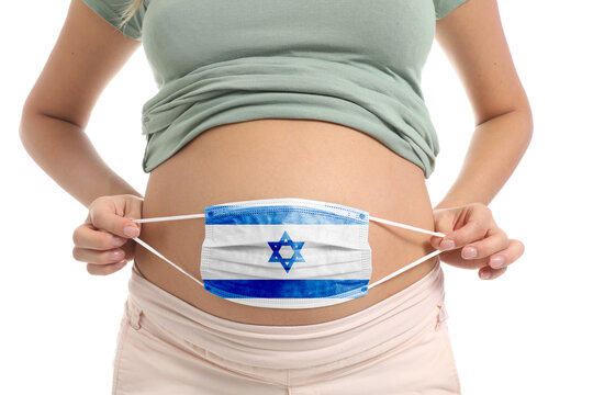 Pregnant woman holding medical mask with painted Israeli flag on white background