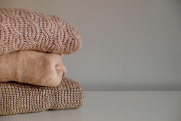 Bunch of knitted warm pastel color sweaters with different knitting patterns folded in stack, clearly visible texture. Stylish fall-winter season knitwear clothing. Close up, copy space for text.