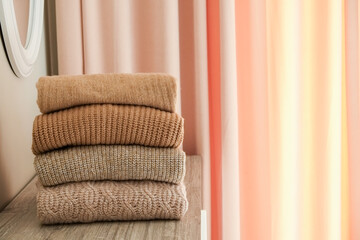 Bunch of knitted warm pastel color sweaters with different knitting patterns folded in stack, clearly visible texture. Stylish fall-winter season knitwear clothing. Close up, copy space for text.