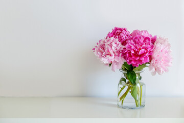 Studio shot of beautiful peony flowers in glass vase on a table over gray wall background with a lot of copy space for text. Feminine floral composition. Close up, backdrop.