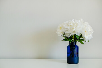 Studio shot of beautiful peony flowers in glass vase on a table over gray wall background with a lot of copy space for text. Feminine floral composition. Close up, backdrop.