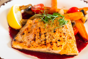A dish of grilled salmon fillet with vegetables on a plate close up.