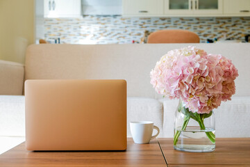 Home office concept. Designated work from home area. Feminine workspace with modern laptop and vase with flowers on table. Close up, copy space, background.