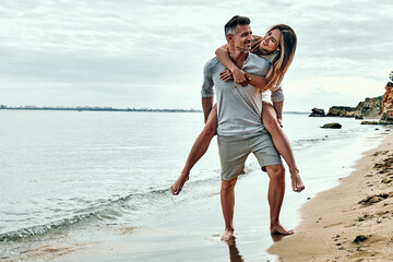 Happy couple in love on beach summer vacations. Joyful woman piggybacking on husband having fun.