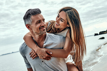 Smiling man giving woman a piggy back at the beach. - Powered by Adobe