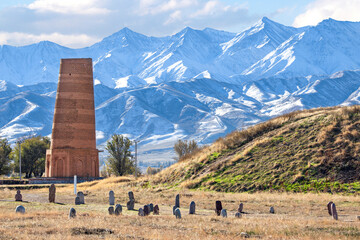 Burana tower which is an old and large minaret in the ruins of the ancient site of Balasagun with tombstones known as Balbas in the foreground, Kyrgyz