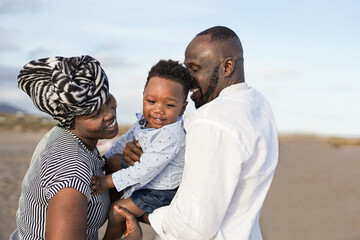 Happy african family enjoy summer vacation with baby on the beach - Black parents having playful time with toddler outdoor