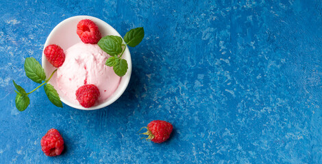 A romantic and delicious dessert. Raspberry ice cream in a white cup with fresh raspberries and a sprig of mint on a blue background. Flat lay. Copy space.