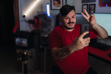 Chico joven gordo con camiseta roja grabando frente a una cámara en un set up gamer