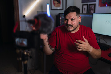 Fototapeta na wymiar Chico joven gordo con camiseta roja grabando frente a una cámara en un set up gamer