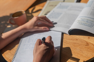 Female hands writing with pen in notebook or planner, taking notes, studying with academic...
