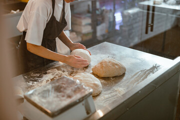 Baker kneads dough for bread at table in craft bakery shop closeup