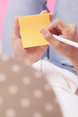 woman writing message on yellow note paper.