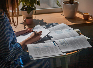 Female hands writing with pen in notebook, taking notes, studying with academic textbook, close up.