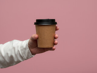 Woman hands hold paper cup on pink background. Copy space.