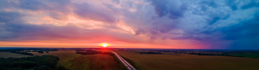 Obraz na płótnie Canvas Panoramic aerial view of highway on red sunset. Landscape with road near countryside fields. Beautiful winding road leading through rural countryside with evening sunlight. Dramatic sky background.