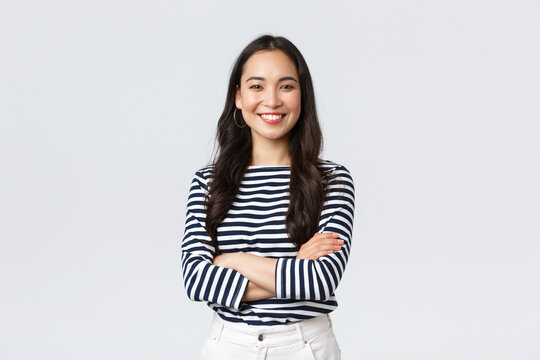 Lifestyle, beauty and fashion, people emotions concept. Young asian female office manager, CEO with pleased expression standing over white background, smiling with arms crossed over chest