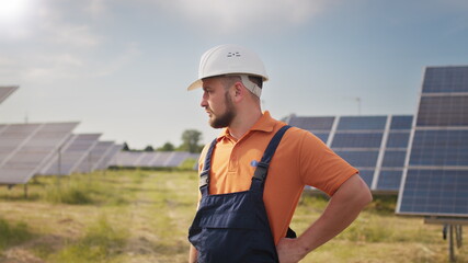 Portrait ecology worker in hard hat standing at solar panel field. Industrial people. Portrait of male engineer in hard helmet turning head and looking to camera. Concept of solar station development