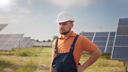 Portrait ecology worker in hard hat standing at solar panel field. Industrial people. Portrait of male engineer in hard helmet turning head and looking to camera. Concept of solar station development