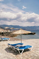 Fototapeta na wymiar Sun loungers with a table stand under a beach umbrella on a cobbled beach