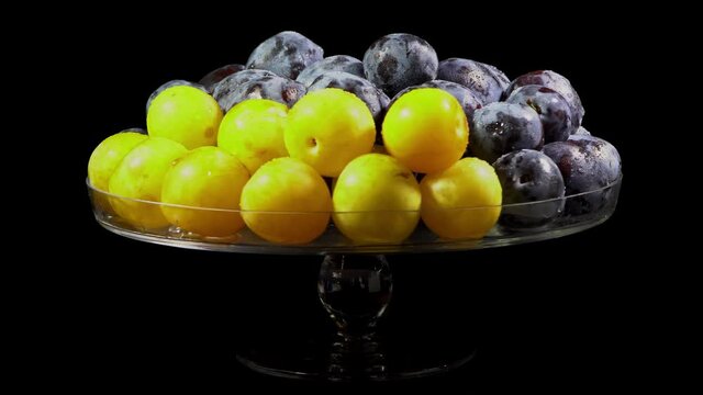 Composition of berries on a rotating table, yellow plum and purple prunes