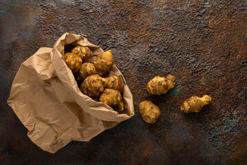 Organic Jerusalem artichoke in paper package on textured background. Autumn harvest of root vegetables. Concept healthy food.