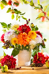 Autumn still life with garden flowers. Beautiful autumnal bouquet in vase on wooden table. Colorful dahlia, chrysanthemum and berries.