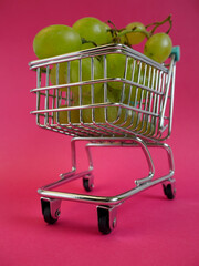 a white grape variety is lying in a supermarket cart on a pink background . bottom view. online shopping