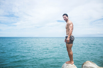 Muscular Hispanic man standing on a rock with turquoise sea in he background