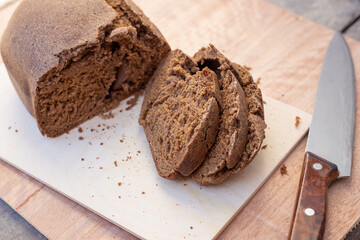 Freshly baked brown Borodino bread bun, cut into slices, next to a large knife. Fresh homemade baked goods. Selective focus.