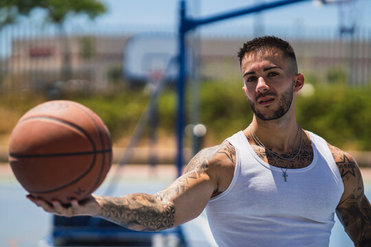 Chico joven tatuado y musculado jugando al baloncesto con el cielo azul despejado 