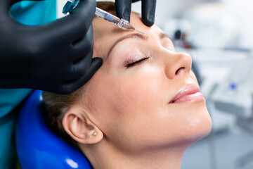 Attractive woman is getting a rejuvenating facial injections. She is sitting calmly at clinic. The expert beautician is filling female wrinkles by hyaluronic acid.