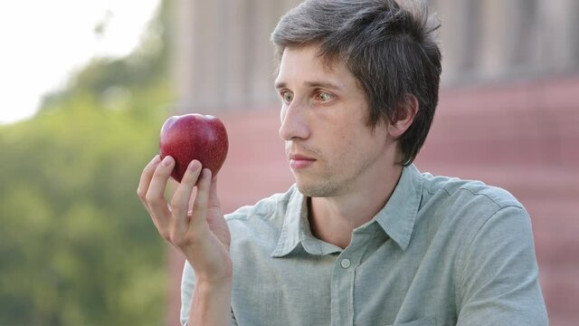 Young millennial man wants to eat apple but cannot. Funny Guy jokes, shows pantomime he can not bite fruit. Vitamins meals, intermittent fasting, carbohydrate-free diet, unattainable goal concept