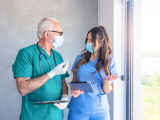Man and women physicians colleagues in uniforms with face masks standing and talking.