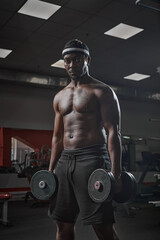 Fototapeta na wymiar African american sports guy bodybuilder with naked muscular torso exercising with dumbbells in gym