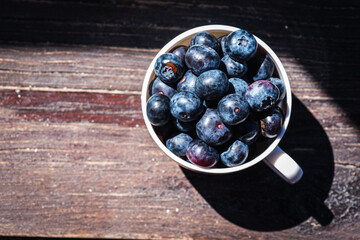 Large, juicy berries, blueberries in a light mug on a gray-cinnamon wooden surface, light shadow, sunbeam. Top view with space for text. Banner