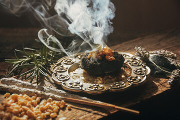 Charcoal burning with incense, incense resin, rosemary, laurel, lavender on a rustic wooden table,...