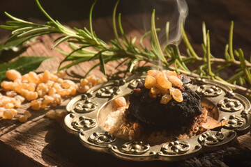Charcoal burning with incense, incense resin, rosemary, laurel, lavender on a rustic wooden table,...