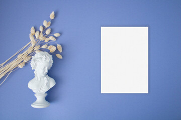 Blank greeting card mock up with dry grass and statue on the blue background
