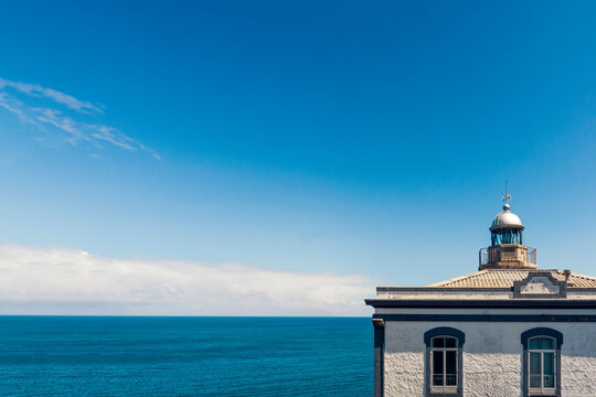 Minimalistic picture of the lighthouse located in Candás, municipality of Carreño, Principality of Asturias Spain. 
Fragment of a historic building above the blue calm sea and sky captured in summer.