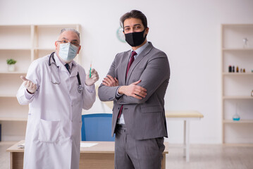 Young businessman visiting old male doctor in vaccination concep