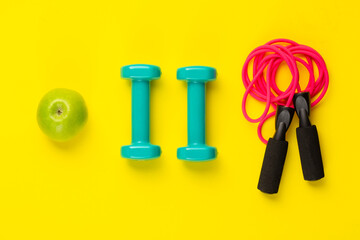 Fitness and sport concept. Jump rope, dumbbells and green apple on bright yellow background.