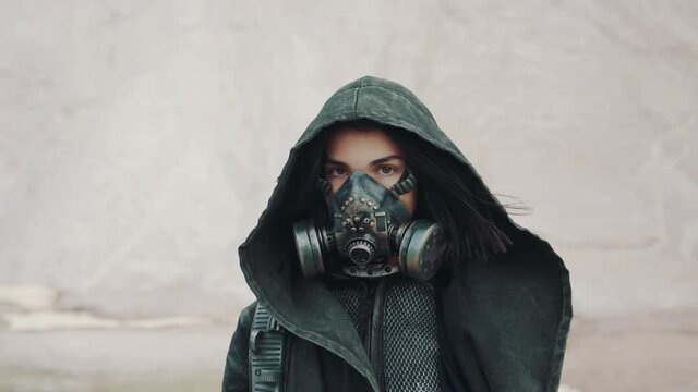 Portrait post apocalyptic woman in grunge clothes hooded mantle and protective gas mask posing by white mountain in desert looking into camera. Future female survivor. Steadicam following shot