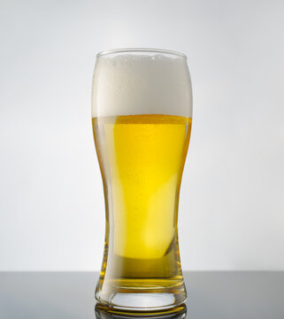 Glass of light beer on a white background. Amber color of the drink and white foam. Minimalism. Single object. There is no one in the photo. Restaurant, bar, pub, advertising.